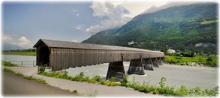 Eine überdachte Holzbrücke ragt über den Rhein.