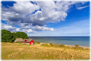 Eine Hütte oder ein Bauernhof am Wasser bei blauem Himmel.